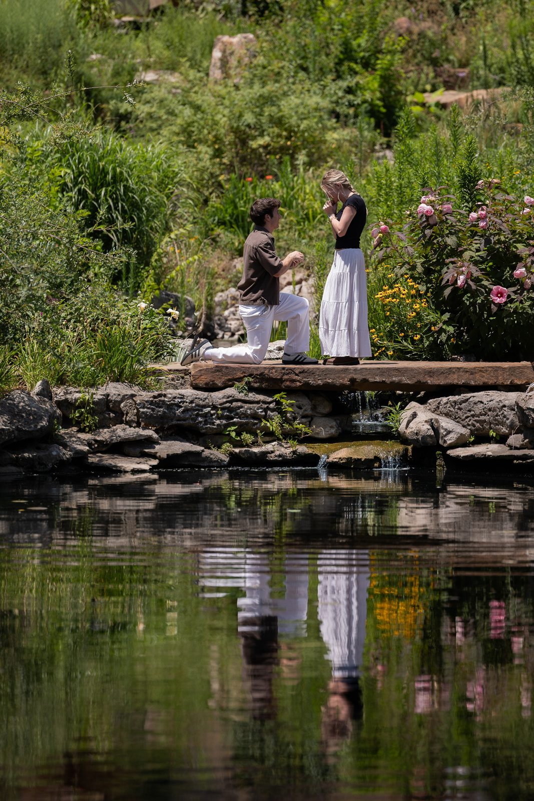 Simon on one knee proposing to Francesca on a garden bridge in Tulsa